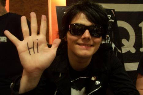 Gerard Way smiling and waving at the camera. 'Hi' is written on his hand.